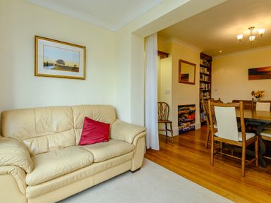 A living room with a beige leather sofa and red cushion next to a dining area with wooden chairs and table at Caradoc Tutshill near Chepstow