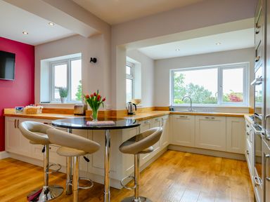 A kitchen with beige cabinets wooden countertops a black round table with stools and windows with outdoor views at Caradoc Tutshill near Chepstow