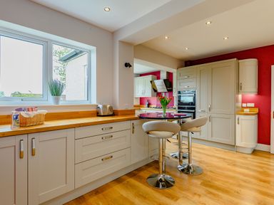 A kitchen with cream cabinets wooden countertops a window two bar stools and a round table at Caradoc in Tutshill near Chepstow