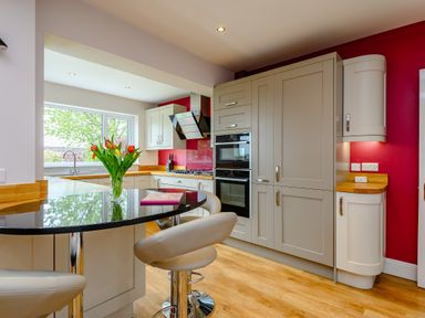 A kitchen with white cabinets a black countertop a vase with flowers and bar stools at Caradoc Tutshill near Chepstow