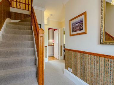 A hallway with carpeted stairs a framed picture and a mirror on the wall at Caradoc in Tutshill near Chepstow