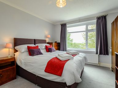 A bedroom with a double bed red and purple cushions bedside tables and a window with curtains at Caradoc Tutshill near Chepstow
