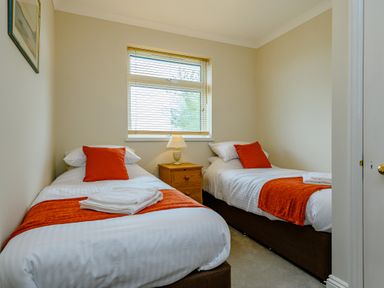 A bedroom with two single beds a wooden nightstand and a window at Caradoc in Tutshill near Chepstow