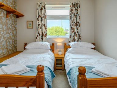 A bedroom with two single beds a nightstand with a lamp and a window with floral curtains at Caradoc Tutshill near Chepstow