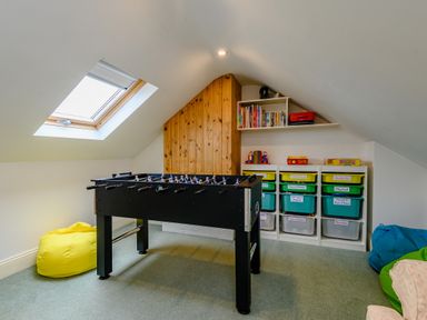 A playroom with a foosball table bean bags and shelves with labeled storage bins at Caradoc Tutshill near Chepstow
