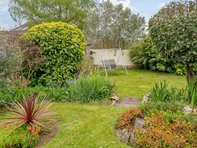 A garden with grass, various plants, shrubs, and a metal garden swing at Caradoc Tutshill near Chepstow