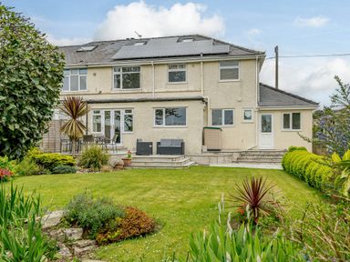 A backyard garden with lawn plants patio furniture and a house with solar panels on the roof at Caradoc Tutshill near Chepstow