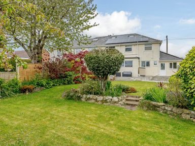 A backyard garden with grass lawn bushes and a two story house with solar panels on roof at Caradoc in Tutshill near Chepstow