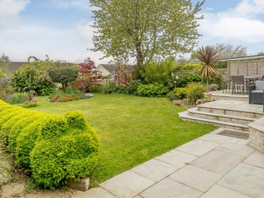 A garden with trimmed bushes trees and a patio area with chairs and table at Caradoc Tutshill near Chepstow