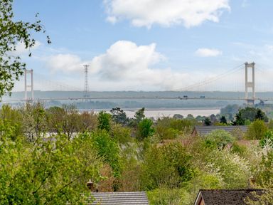 A view of a suspension bridge over a river with trees and rooftops in the foreground at Caradoc Tutshill near Chepstow