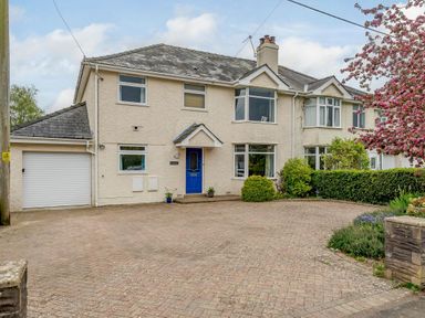 A semi detached house with a blue door a garage and a driveway with bushes and a tree at Caradoc Tutshill near Chepstow