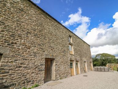Exterior view of a stone building with wooden doors and windows under a blue sky at Hollowgill Barn in Sedbergh
