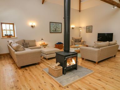 A living room with beige sofas a wood burning stove and a television at Hollowgill Barn in Sedbergh