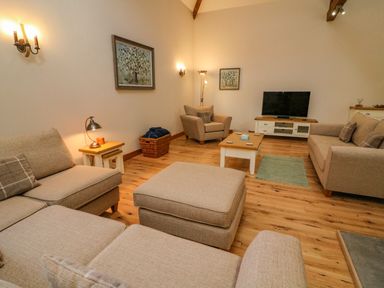 A living room with beige sofas and armchairs wooden floor and a television on a cabinet at Hollowgill Barn Sedbergh