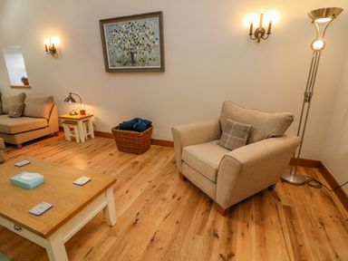 A living room with beige armchair sofa wooden coffee table and a painting on the wall at Hollowgill Barn in Sedbergh