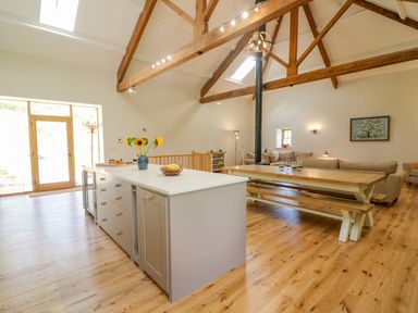 An open kitchen and living area with wooden beams a kitchen island and a dining table with benches at Hollowgill Barn in Sedbergh