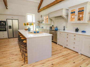 A kitchen with a large island and bar stools with sunflowers on the island at Hollowgill Barn in Sedbergh