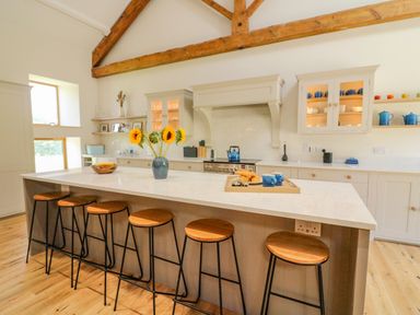 A kitchen with wooden stools around an island with flowers and cups at Hollowgill Barn in Sedbergh