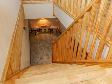 A staircase with wooden handrails leading to a small sitting area with two chairs a table and a lamp at Hollowgill Barn in Sedbergh