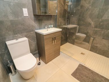 A bathroom with a toilet sink cabinet shower area and floor mat at Hollowgill Barn in Sedbergh