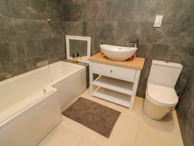 A bathroom with a bathtub sink on wooden vanity and toilet at Hollowgill Barn in Sedbergh