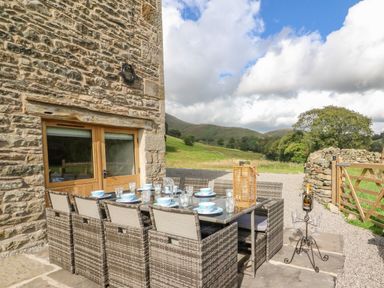 An outdoor dining area with a table set with dishes and chairs next to a stone building at Hollowgill Barn in Sedbergh