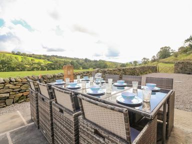 An outdoor dining table with chairs set with plates bowls and glasses near a stone wall with countryside view at Hollowgill Barn in Sedbergh