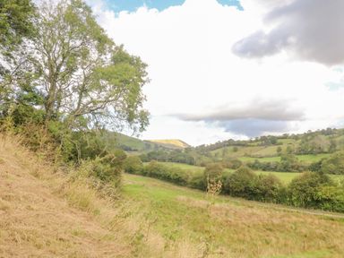 A rural landscape with trees grass fields and hills under a partly cloudy sky at Hollowgill Barn in Sedbergh