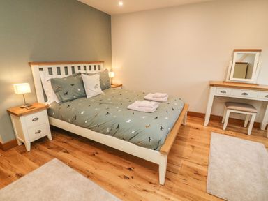 A bedroom with a bed with animal print bedding bedside tables with lamps a dressing table and stool on a wooden floor at Hollowgill Barn in Sedbergh