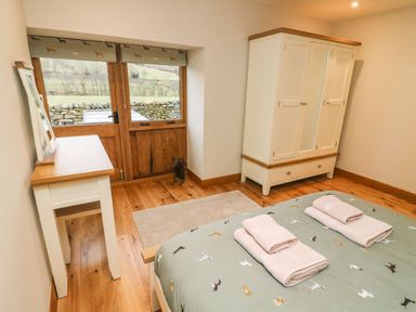 A bedroom with a bed and folded towels on it a wardrobe a table and wooden double doors with a view of a stone wall and fields at Hollowgill Barn in Sedbergh