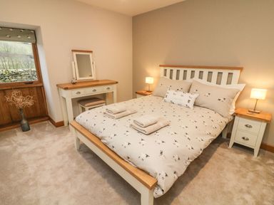 A bedroom with a bed with sheep patterned bedding two bedside tables with lamps a dressing table and a window with wooden blinds at Hollowgill Barn in Sedbergh