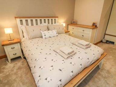 A bedroom with a bed with sheep patterned bedding two bedside tables with lamps and a chest of drawers at Hollowgill Barn in Sedbergh