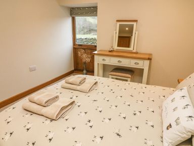 A bedroom with a bed having sheep patterned bedding and towels on it next to a dressing table with a mirror at Hollowgill Barn in Sedbergh