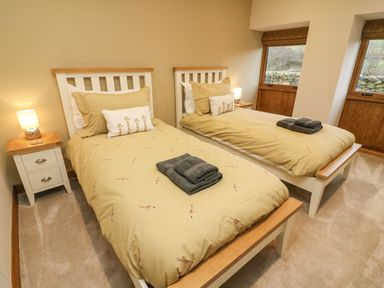 A bedroom with two single beds with beige bedding and giraffe pillows and bedside tables with lamps at Hollowgill Barn in Sedbergh