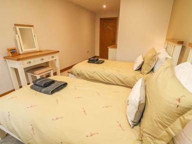 A bedroom with two single beds with yellow bedding and a dressing table with a mirror at Hollowgill Barn in Sedbergh