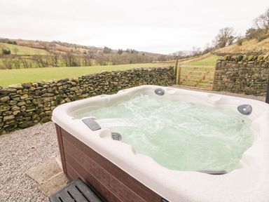 An outdoor hot tub with bubbling water next to a stone wall and wooden gate in a rural area at Hollowgill Barn in Sedbergh