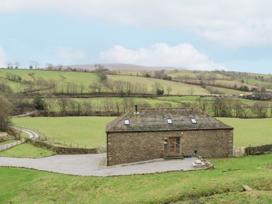 A stone barn with a tiled roof in a rural area with green fields and hills around at Hollowgill Barn in Sedbergh