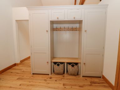 A built in storage unit with cabinets drawers hooks a bench and two baskets on a wooden floor at Hollowgill Barn in Sedbergh