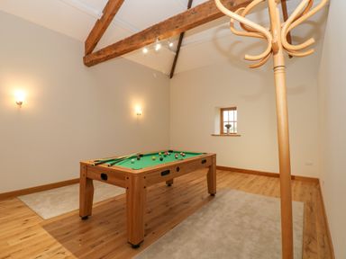 A game room with a pool table and wooden coat rack under exposed ceiling beams at Hollowgill Barn in Sedbergh