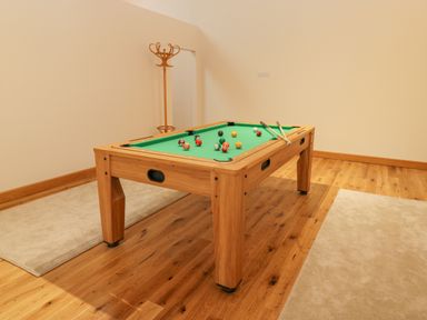 A room with a pool table, cue sticks, and a coat rack at Hollowgill Barn in Sedbergh