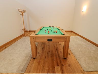 A pool table with billiard balls and cues in a room with wooden floors two rugs and a wooden coat rack at Hollowgill Barn in Sedbergh