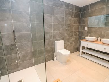 A bathroom with a toilet shower area and double sinks with a large mirror at Hollowgill Barn in Sedbergh