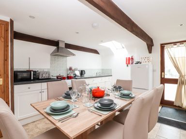 A kitchen and dining area with a wooden table set with plates glasses and cutlery at Wheal Prosper@The West Dry in St Austell