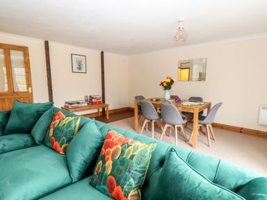 A living room with a green sofa and colorful pillows next to a wooden dining table with grey chairs at Wheal Prosper@The West Dry in St Austell