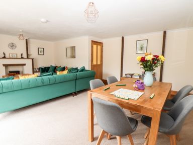 A living room with green sofas a wooden dining table with chairs and a vase of flowers a Scrabble game on the table and a fireplace at Wheal Prosper@The West Dry in St Austell