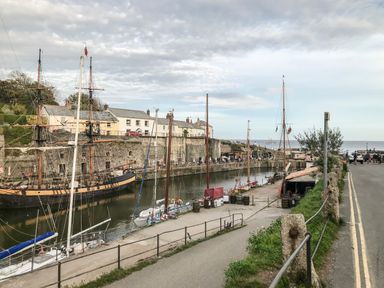 A harbor with sailing ships docked near a stone wall and houses by the water at Wheal Prosper@The West Dry in St Austell