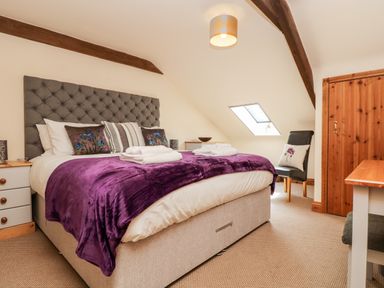 A bedroom with a bed with purple blanket and pillows a chair a wooden door and a skylight at Wheal Prosper@The West Dry in St Austell
