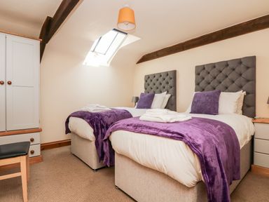 A bedroom with two single beds purple throws and pillows a skylight and wooden beams at Wheal Prosper@The West Dry in St Austell