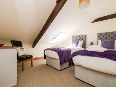 A bedroom with two single beds with purple throws and pillows a black chair a white dresser and a skylight window at Wheal Prosper@The West Dry in St Austell