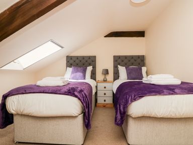 A bedroom with two single beds with purple throws and pillows between two wooden beams at Wheal Prosper@The West Dry in St Austell